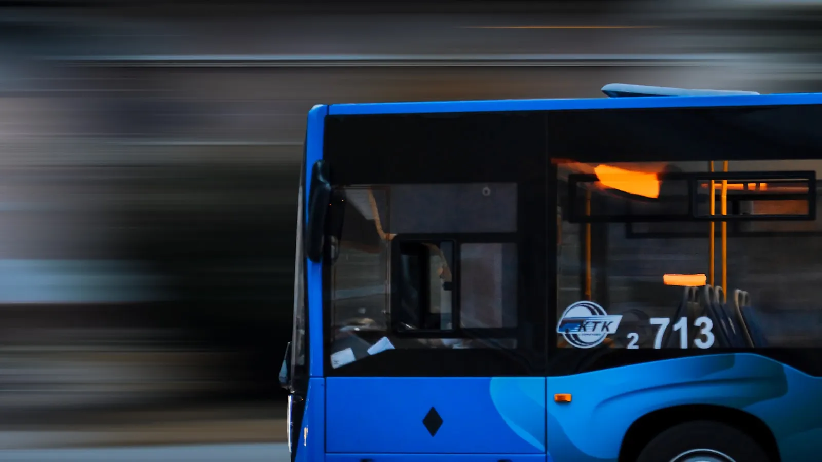 A blue city bus driving along a street beside tall buildings