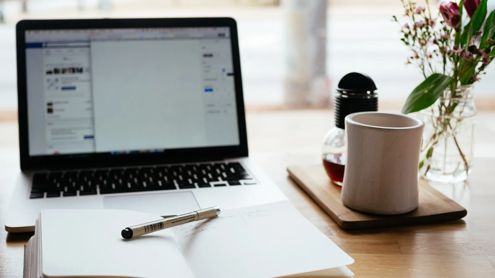 An open laptop beside a notebook and study materials on a desk